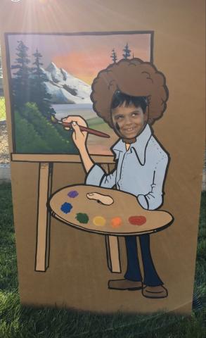 A student in a photo prop of Bob Ross painting happy trees. 