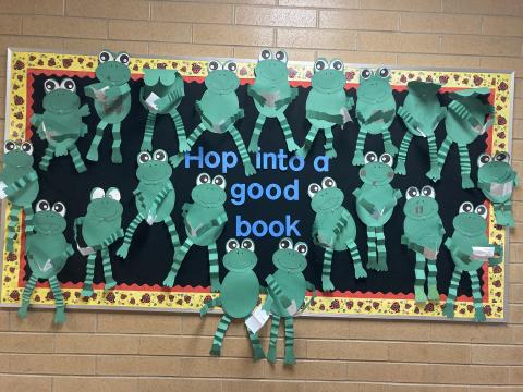 Bulletin board of frogs reading books with the caption Hop into a good book