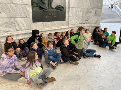 Students sitting on the marble floor during a tour of the Capitol