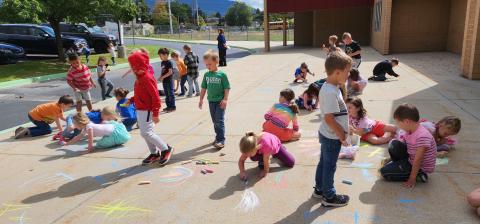 Kindergarten students doing chalk art on the sidewalk 