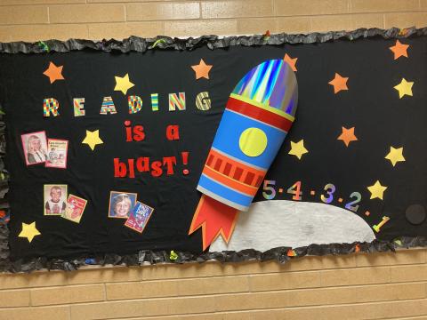 Library Bulletin Board Reading is a blast with a rocket ship, stars and three pictures of staff and their favorite book