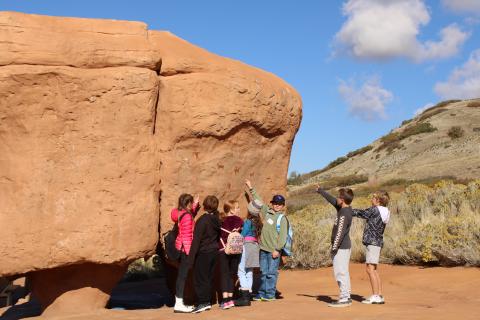 A group of students pointing out a fossil on a rock 