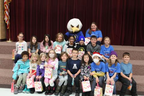Students sitting on the steps of the stage with ACE the Eagle with their goody bags. 