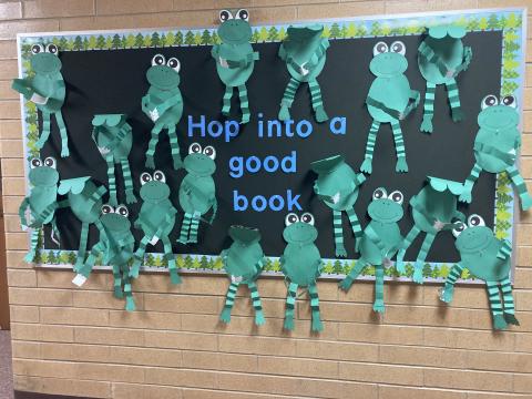 Bulletin board of frogs reading books with the caption Hop into a good book