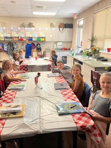 Students seated at a table as if to eat dinner tasting books
