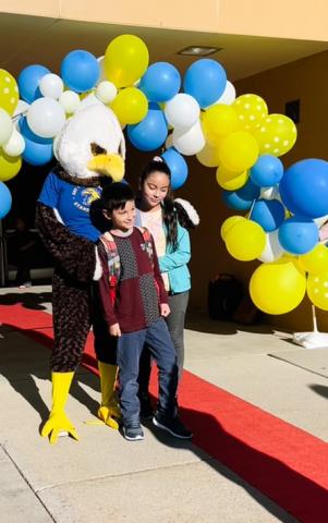 The Art City Eagle standing with students on the red carpet under the balloon arch