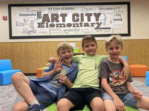 Three Boys sitting on a bench in front of the Art City Elementary picture