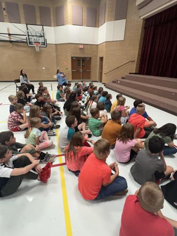 Students sitting on the floor, anxiously engaged in what is going on in front of them