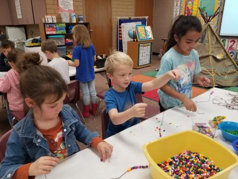 Kindergarten students making beaded necklaces
