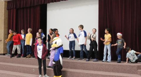 Students dancing on the stage before an assembly with Ace the Eagle