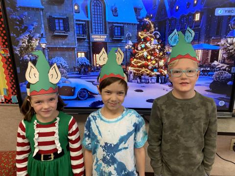 Students dressed like Elves posing in front of a Christmas scene. 