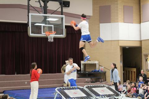 Member of the Dunk team soaring through the air over two teachers