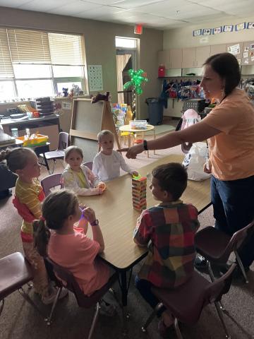 A parent helper teaching Kindergarten students how to play Jenga