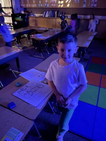 Kindergarten student doing math on a white board with black lights on. 