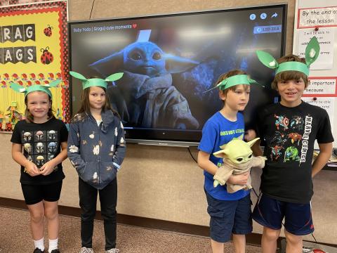 Four students with Yoda ears in front of a picture of Grogu