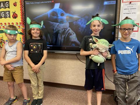 Four students with Yoda ears in front of a picture of Grogu and one holding a stuffed Grogu