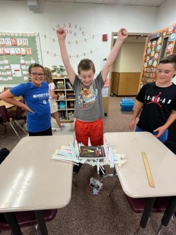 Three students showing off their bridge made of straws