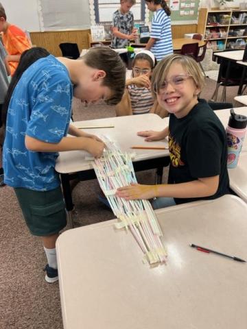 Two students working on their bridge made of straws