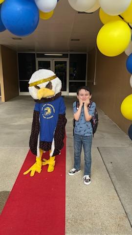 The Art City Eagle standing with a student on the red carpet under the balloon arch 