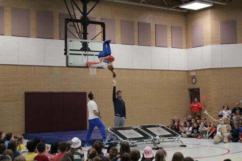 BYU Dunk team "flying" through the air, over Mr. Cornwall, as students cheer them on. 