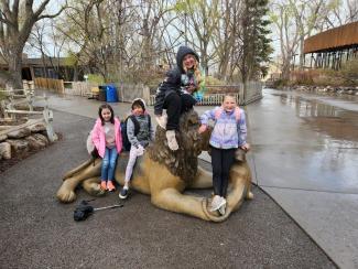 Students posing on a lion statue at the zoo