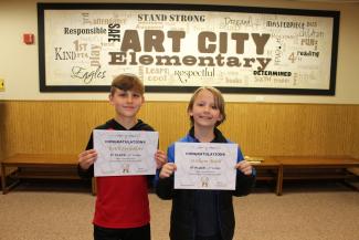 Two fourth grade students holding certificates of awards for 8th and 9th place