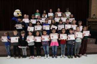 Stand strong students standing on the steps of the stage holding their Student of the month certificate with ACE the Eagle