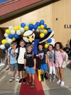 The Art City Eagle standing with students on the red carpet under the balloon arch 