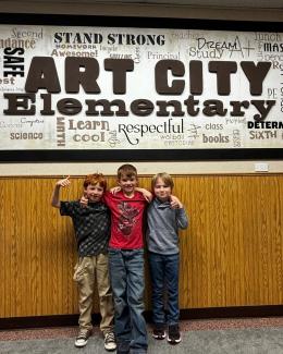 Three boys standing in front of the Art City Wall 
