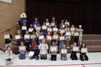 Students standing on the stage steps holding their certificates with ACE the Eagle