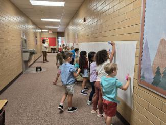 Kindergarten students drawing on paper on the wall