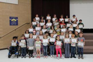 Stand strong students standing on the steps of the stage holding their Student of the month certificate 